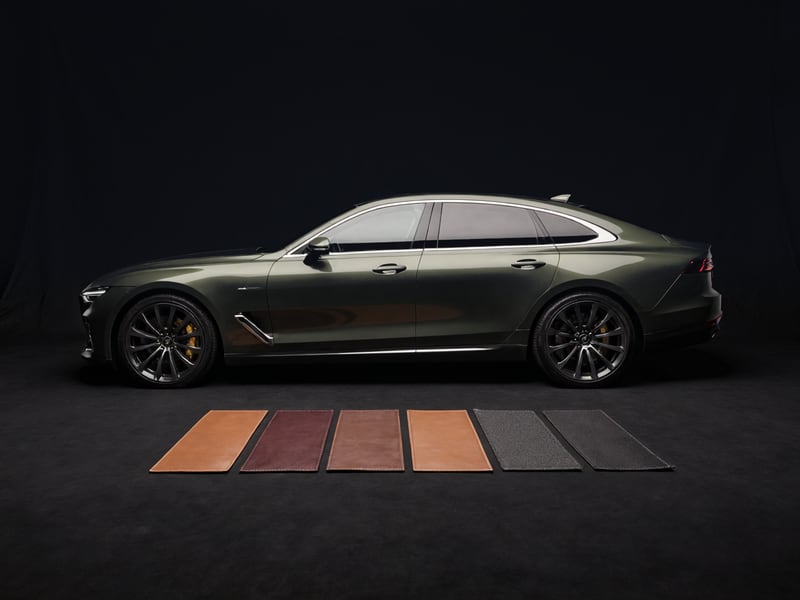 A grand tourer in profile on a dark stage, with a row of leather and textile finish samples laid out in front of it.